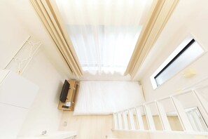 Ein Zimmer mit Dachfenster, einem kleinen Fenster, einem weißen Kinderbett und einem Holzschrank.