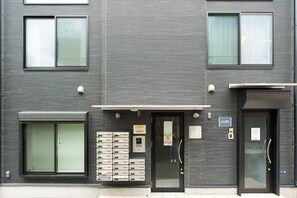 Ein modernes Gebäude mit großem Schiebetür-Eingang, einem Briefkasten und einem Schild, das auf ein Unternehmen hinweist.