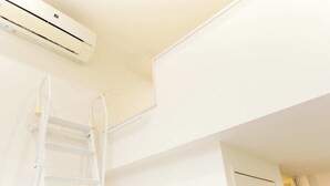Un equipo de aire acondicionado blanco montado en una pared, una escalera blanca apoyada contra la pared, y una puerta blanca al fondo.