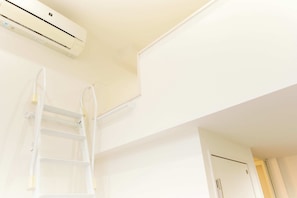 Een witte airconditioningunit bevestigd aan een muur, een witte ladder die tegen de muur leunt en een witte deur op de achtergrond.