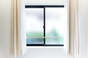 Een kamer met een groot raam, voorzien van een schuifdeur, gordijnen en uitzicht op een groen gebied buiten.