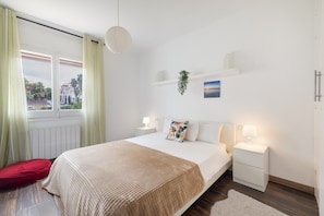 A bedroom with a bed, bedside tables, a window with curtains, a plant, and a painting on the wall. - Apartment 'Melody' in Central Sitges with Private Terrace, Wi-Fi, and Air Conditioning (Sitges)