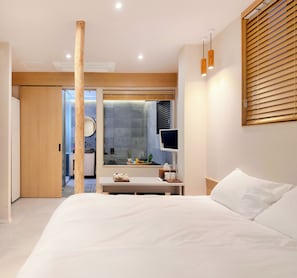 A modern bedroom with a large bed, a desk with a computer, and a view of a cityscape through a window. - whalero (Seoul)