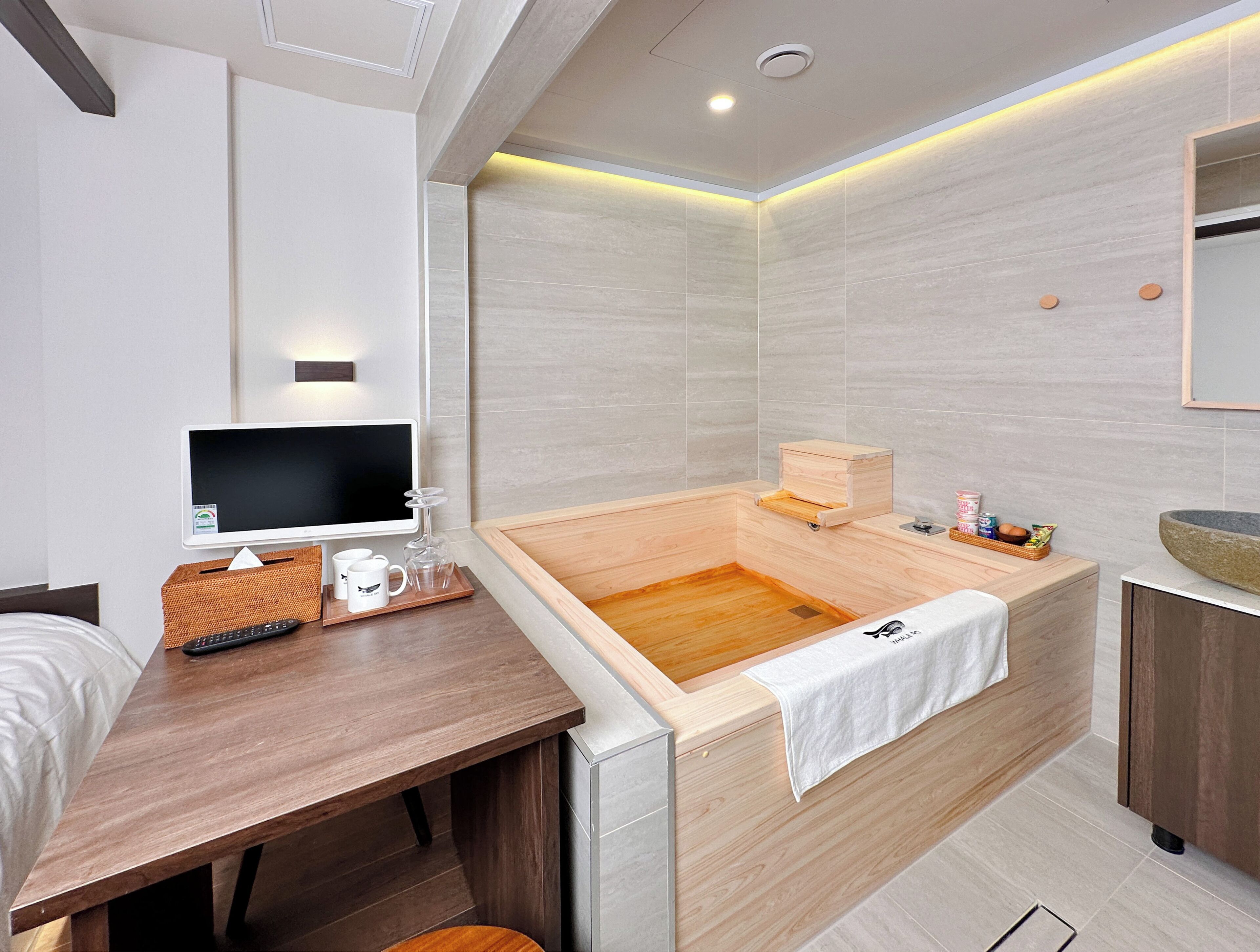 Un baño moderno con una bañera de madera, un tocador de madera, un lavamanos y un televisor sobre una mesa de madera.