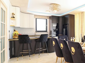 Une cuisine moderne avec un îlot central, des tabourets de bar noirs et un lustre.