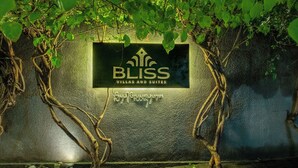 Schild für 'BLISS Villas and Suites' mit strukturierter Wand und Efeu.