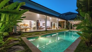 Ein modernes Haus mit Swimmingpool, Sitzgelegenheiten im Freien und tropischen Pflanzen.