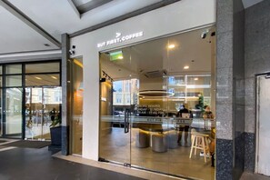 A coffee shop with a glass facade, a sign indicating store hours, and a seating area with stools. - StayHere Relax & Retreat in Viceroy McKinley Hill (Taguig)