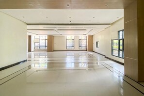 Eine geräumige, gut beleuchtete Hotelhalle mit poliertem Boden, großen Fenstern und einem modernen Deckenstil.