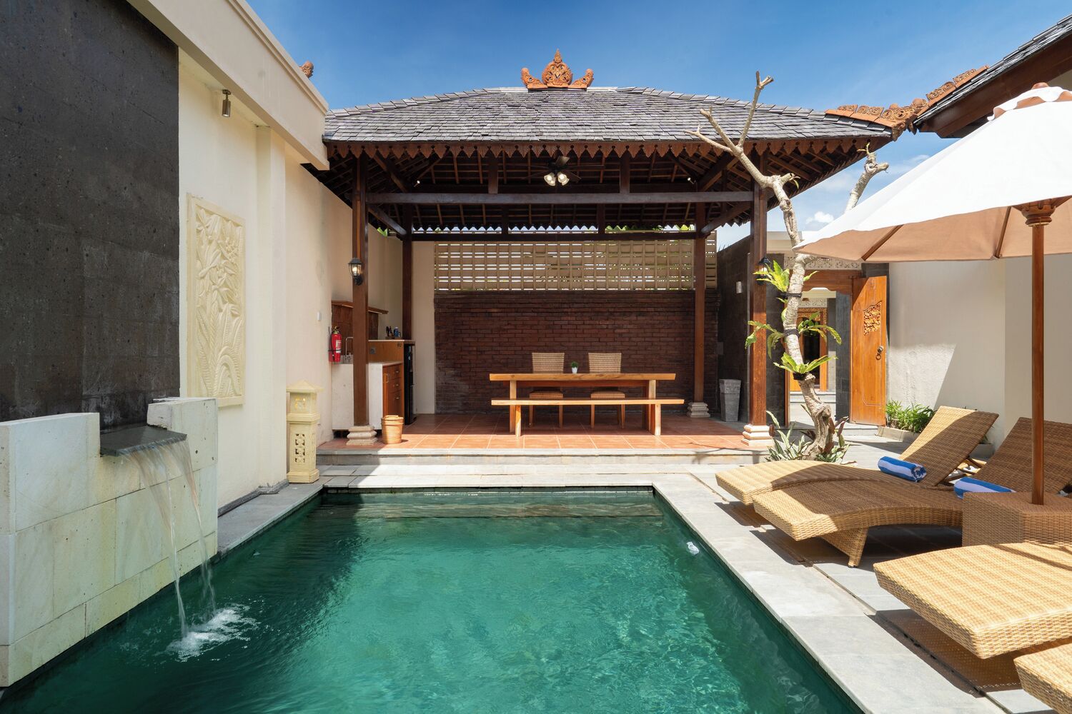 Une piscine avec une terrasse en bois, un espace salon couvert et des chaises longues.