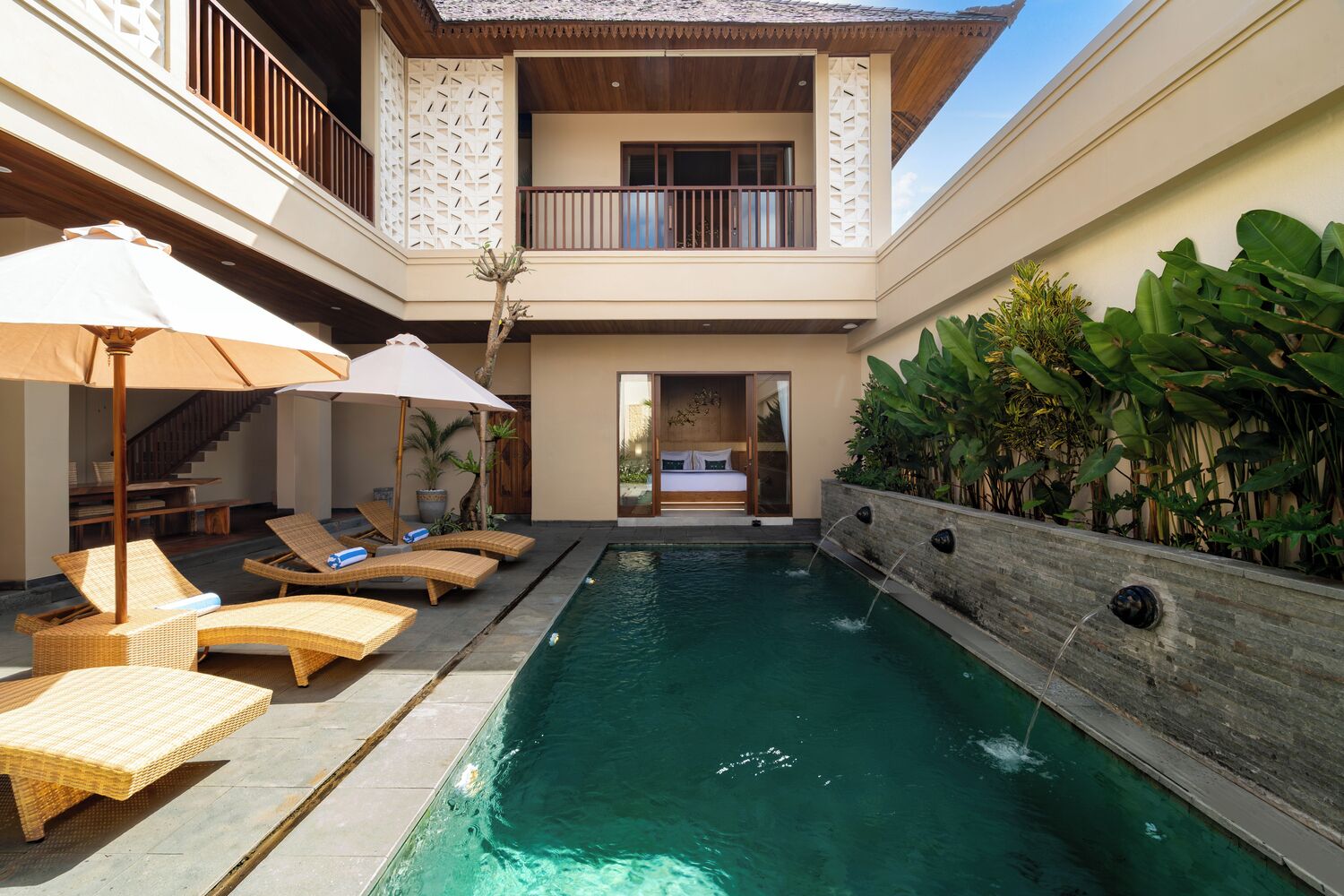 A pool area with lounge chairs and umbrellas, a staircase, and a bedroom with a balcony.