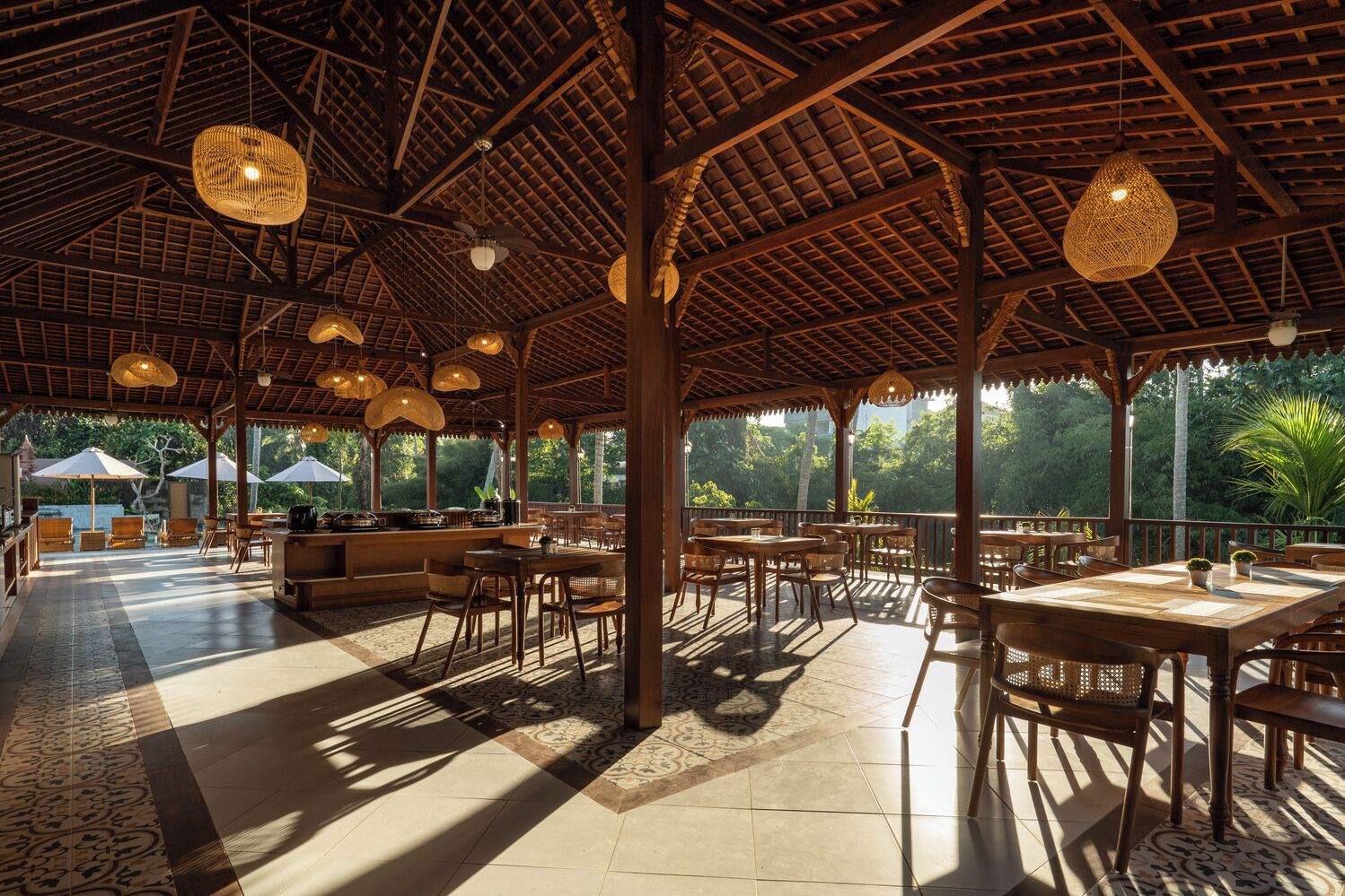 An open-air dining area with wooden beams, wicker furniture, and hanging light fixtures.