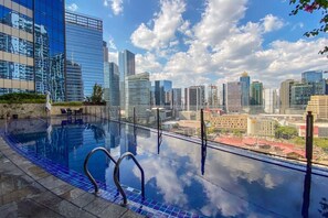 Ein Infinity-Pool auf dem Dach mit Blick auf eine Stadtlandschaft, umgeben von modernen Gebäuden.