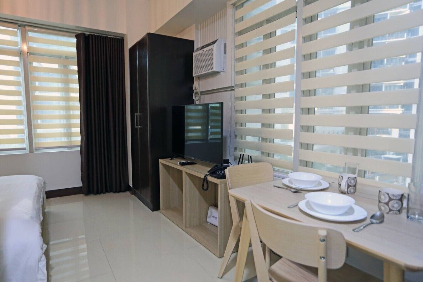 Habitación de hotel con cama, escritorio con televisor, teléfono y mesa de comedor con platos y cubiertos.