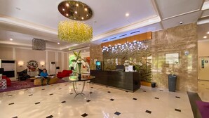 Een hotel lobby met een receptiebalie, een zithoek en een grote kroonluchter.