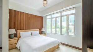 Een moderne slaapkamer met een groot bed, een wand van houten panelen, nachtlampjes en een raam met uitzicht op de stad.