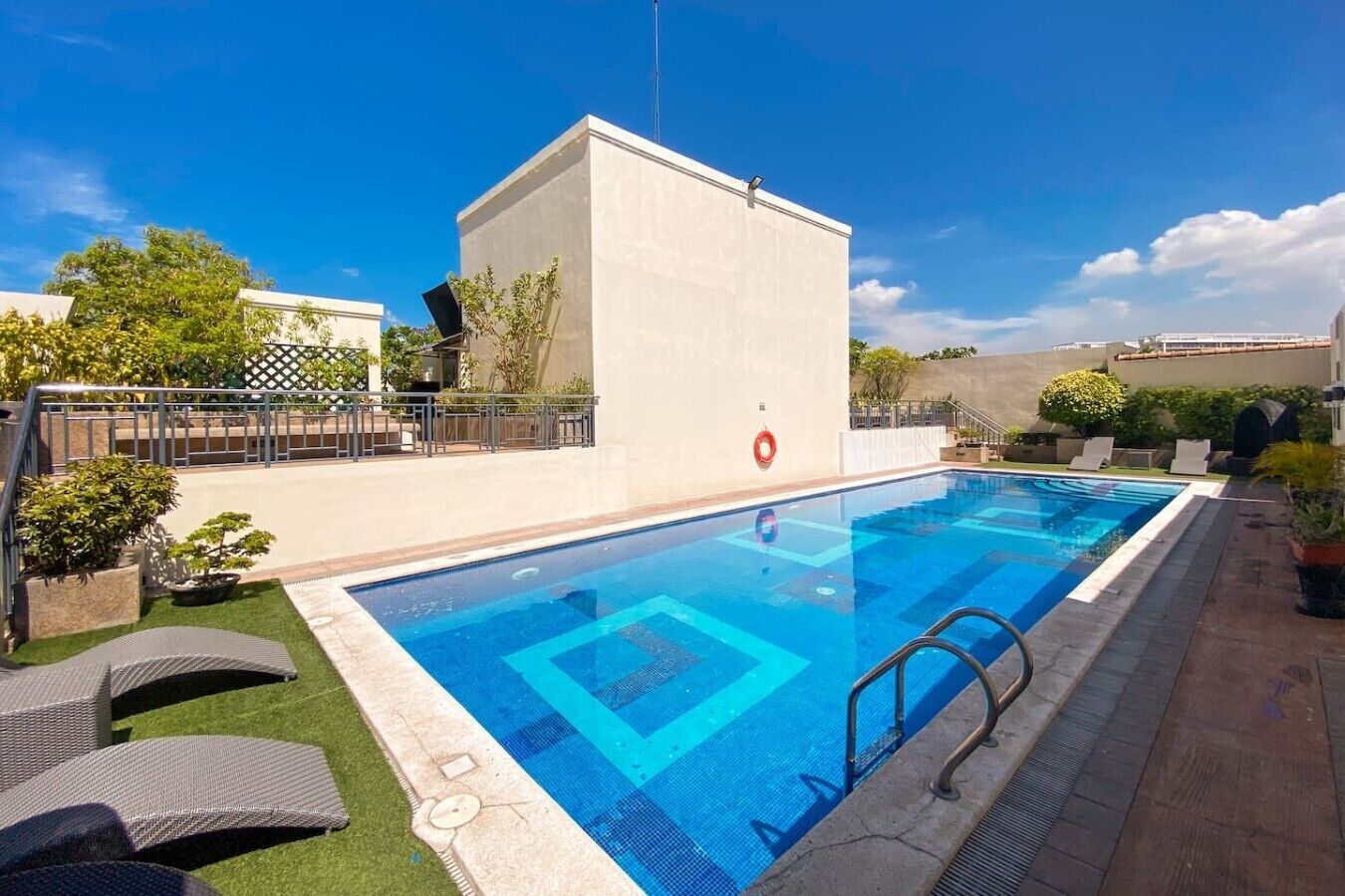 Una piscina rectangular con un flotador salvavidas, rodeada de una zona con tumbonas y un pequeño jardín.