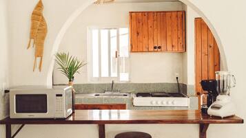 Una cocina con microondas, tostadora, estufa y licuadora en la encimera, armarios de madera, una ventana y una planta.