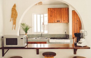 A kitchen with a microwave, toaster, stove, and blender on the counter, wooden cabinets, a window, and a plant.