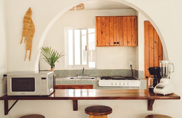 Una cocina con microondas, tostadora, estufa y licuadora en la encimera, armarios de madera, una ventana y una planta.