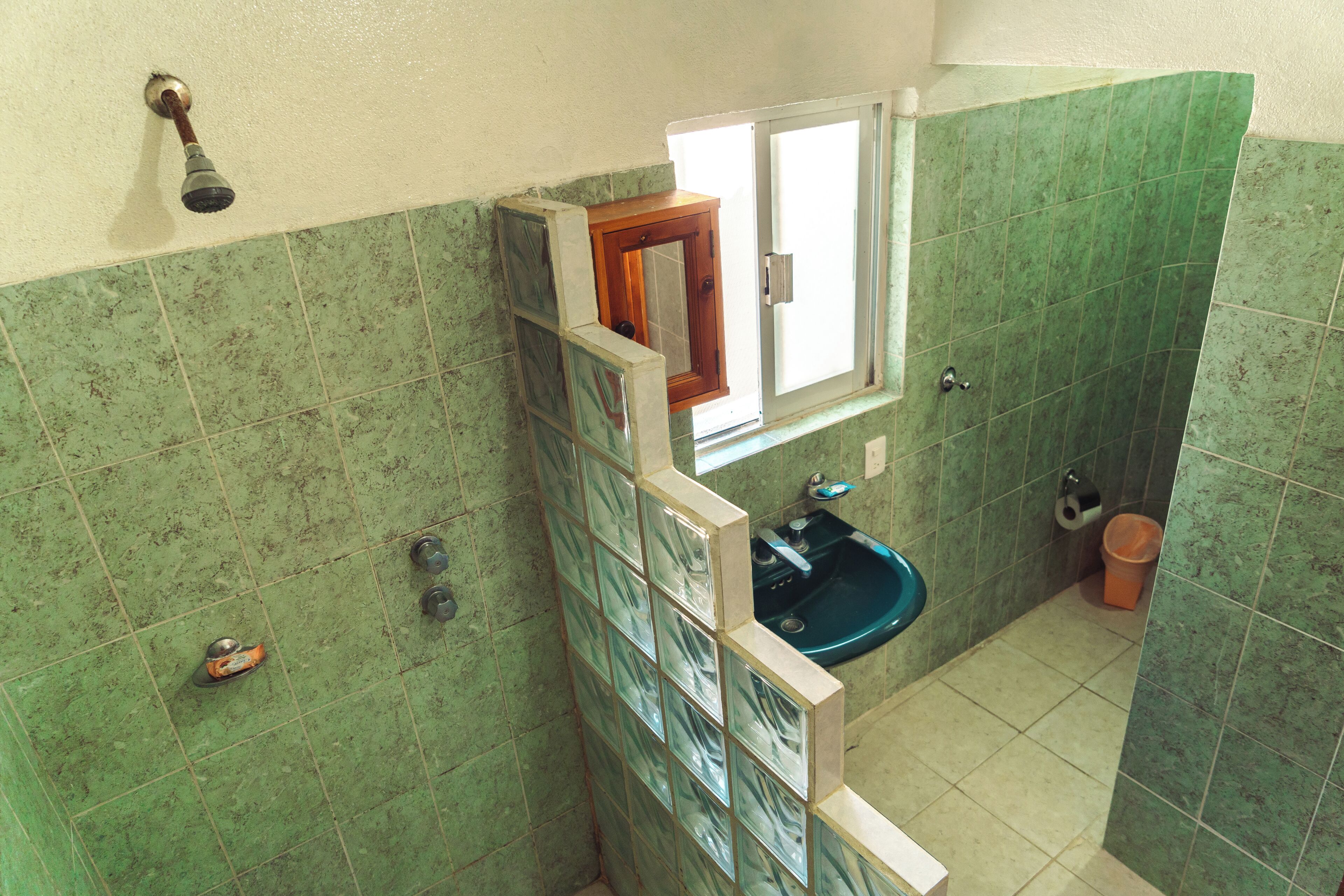 A bathroom with green tiles, a window, a sink, and a shower.