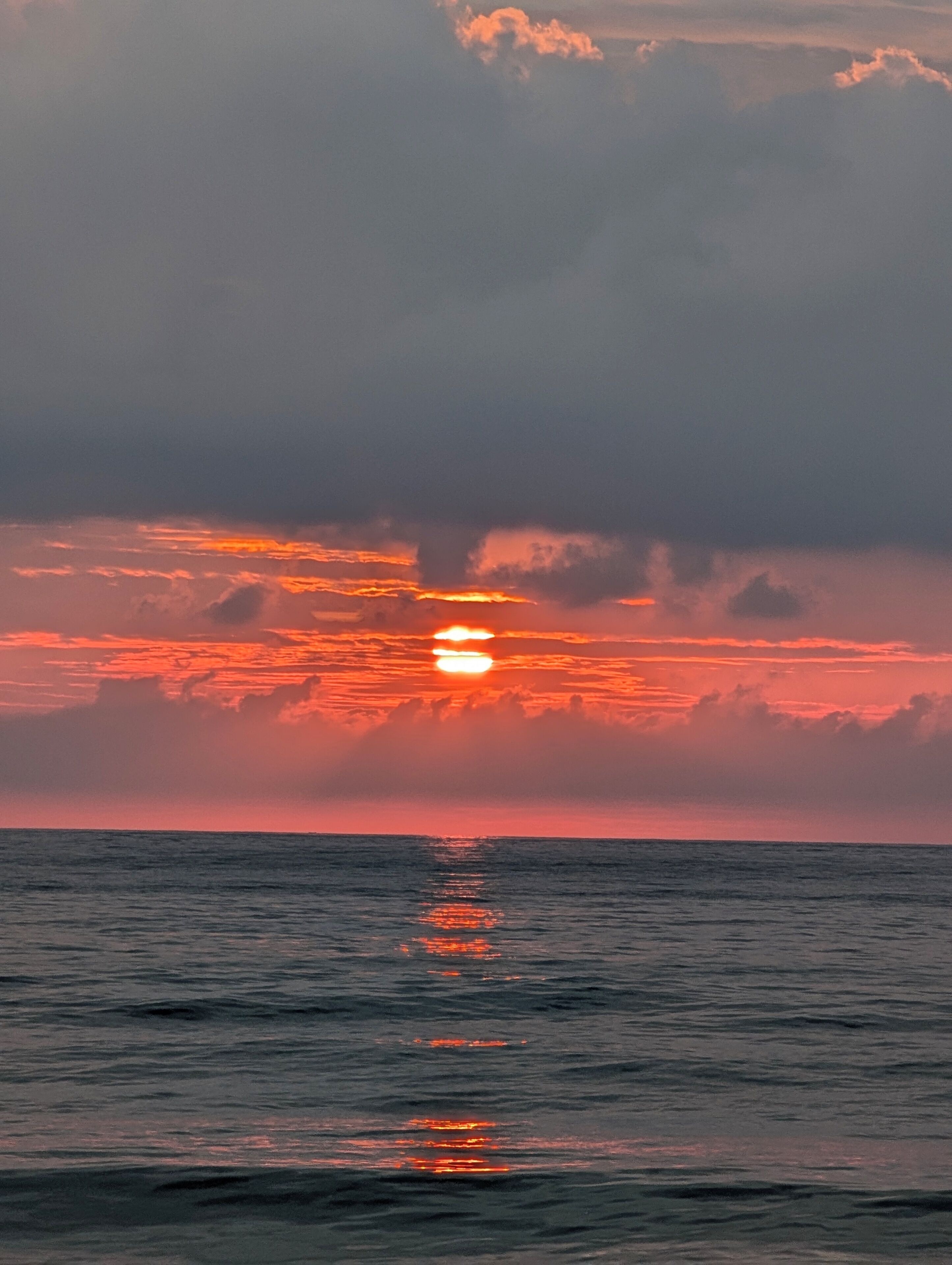 A sunset over the ocean with clouds reflecting on the water.