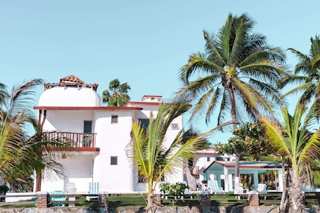 A white building with a balcony, surrounded by palm trees and a clear blue sky.. Villas Malaki