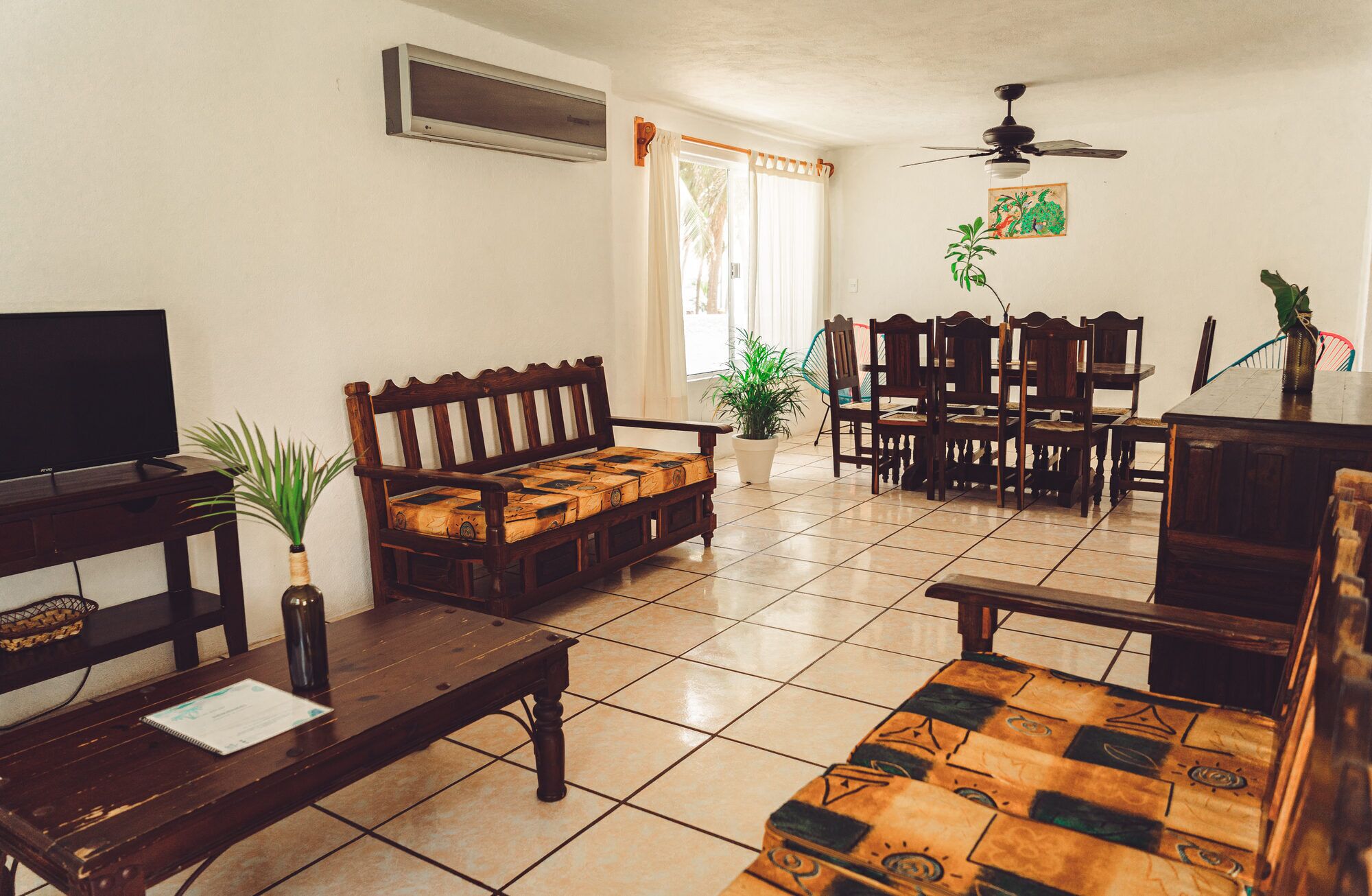 A living room with a television, wooden furniture, a ceiling fan, and a dining area with chairs and a table.