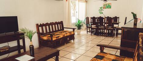 A living room with a television, wooden furniture, a ceiling fan, and a dining area with chairs and a table.