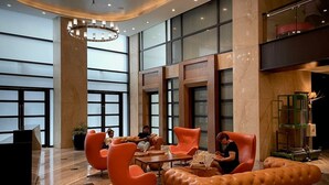 A lobby with a modern design, featuring a seating area with orange chairs and a leather sofa, a reception desk, and large windows. - StayHere Fast WiFi 5 Star View in Makati (Makati)