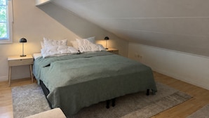 Ein Schlafzimmer mit einem Bett, zwei Nachttischen, einem Fenster und einer schrägen Decke.