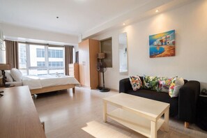 Ein Hotelzimmer mit Bett, Sofa, Couchtisch, Lampe, Stehlampe, einem Gemälde und einem Fenster mit Vorhängen.