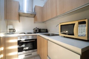 A modern kitchen with stainless steel appliances, wooden cabinets, and a microwave. - StayHere BGC City Studio in SOMA near SM Aura (Fort Bonifacio Global City, Taguig City)