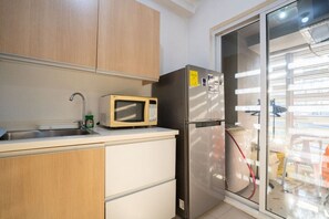 Eine Küche mit Holzausstattung, einer Mikrowelle, einem Edelstahlkühlschrank, einem Waschbecken und einem Fenster mit Jalousien.
