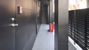 A corridor with a tiled floor, a door with a handle, and a red box on the floor. - Stylewood Nishi-Shinjuku 2 (Shibuya)