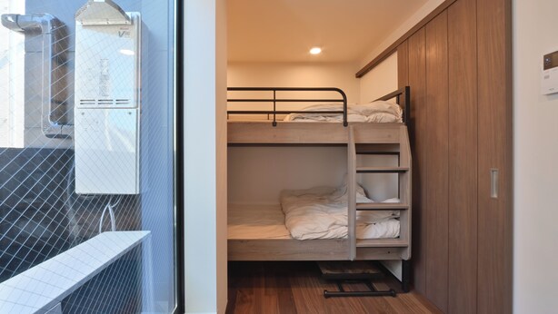 A bunk bed room with a wooden wardrobe and a window with a metal grill. - Stylewood Nishi-Shinjuku 2 (Shibuya)