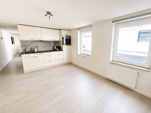 A modern kitchen with light wood flooring, white cabinetry, a built-in oven, and a window with a view. - Central Ghent | Comfortable Rooms with WiFi (Ghent)