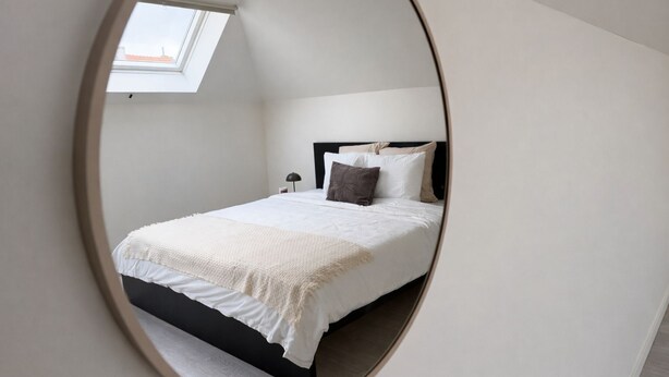 Een slaapkamer met dakraam, een bed met witte beddengoed, een zwart hoofdeinde en een nachtkastje met lamp.