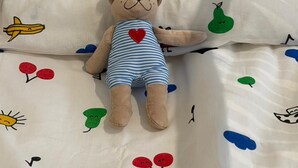 Een bed met een zacht knuffeldiertje en een laken met motieven van fruit en wolken.