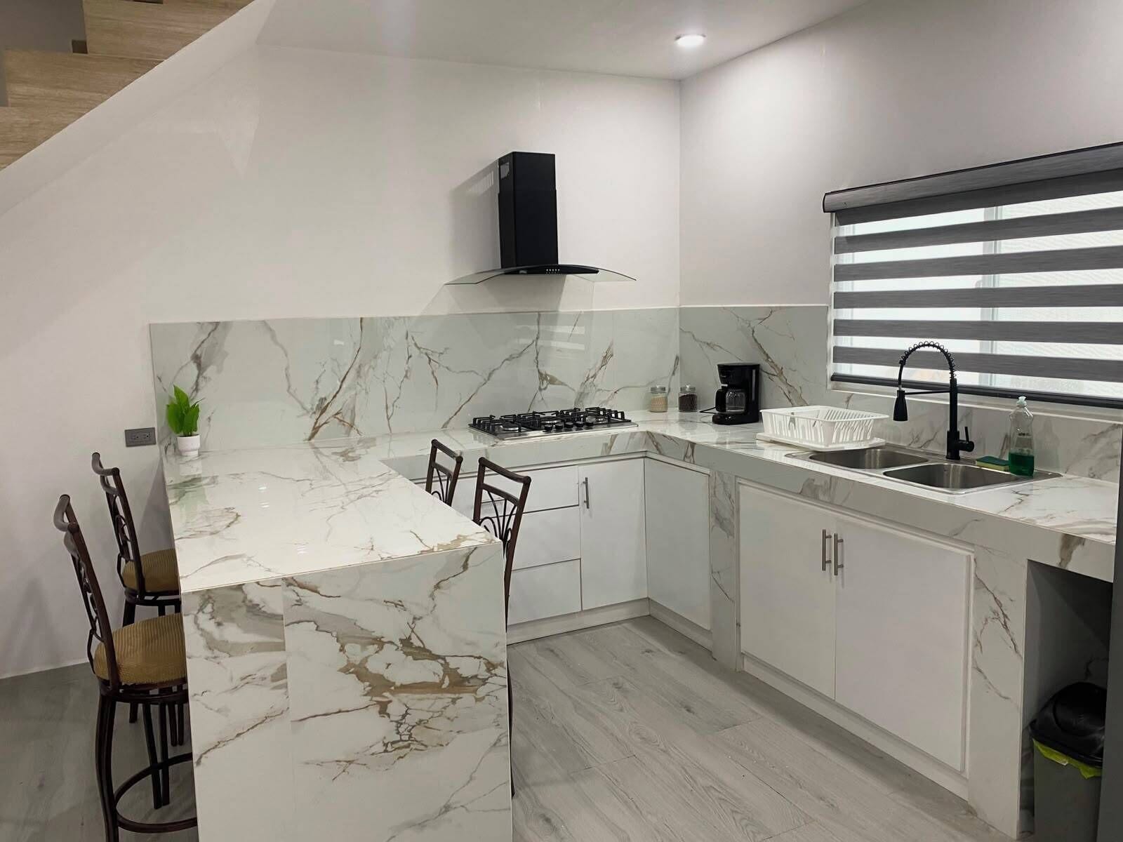 A modern kitchen with a marble countertop, a gas stove, a coffee maker, and a sink with a faucet.. Casa las bugambilias