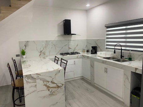 A modern kitchen with a marble countertop, a gas stove, a coffee maker, and a sink with a faucet.. Casa las bugambilias