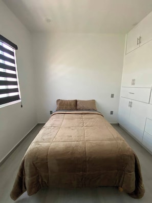 Une chambre à coucher avec un lit, une fenêtre avec des stores et une armoire.