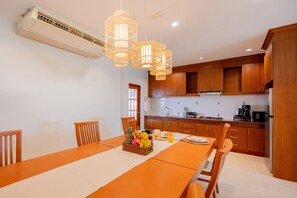 A modern kitchen with wooden cabinets, a dining table with chairs, and a fruit basket.