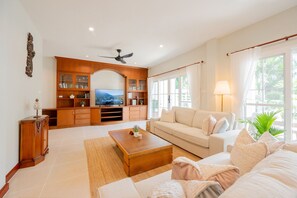 A living room with a sofa, coffee table, TV, wooden entertainment unit, and a ceiling fan.