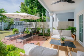 A patio with outdoor furniture, including lounge chairs and a table, surrounded by greenery and a fence. - Renovated 3BR Beach House, 7-Min Walk to Kamala Beach! (Kathu / Kamala)