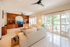 A spacious living room with a sofa, TV, wooden cabinets, and a balcony with curtains.
