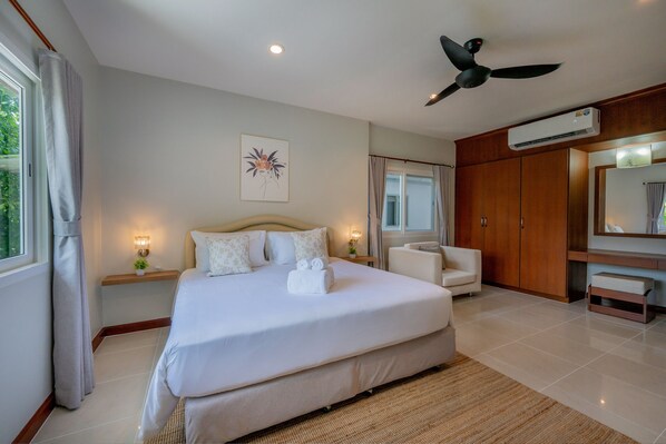 A hotel room with a large bed, a ceiling fan, an air conditioning unit, a TV, and a window with curtains.