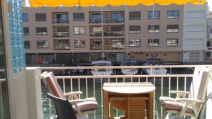 Een balkon met twee stoelen en een tafel, met uitzicht op een jachthaven vol boten en een gebouw met meerdere balkons.
