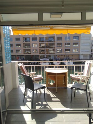A balcony with two chairs and a table, overlooking a marina with boats and a building with multiple balconies. - Apartment 2 bedrooms 1 Living room with balcony (Empuriabrava)
