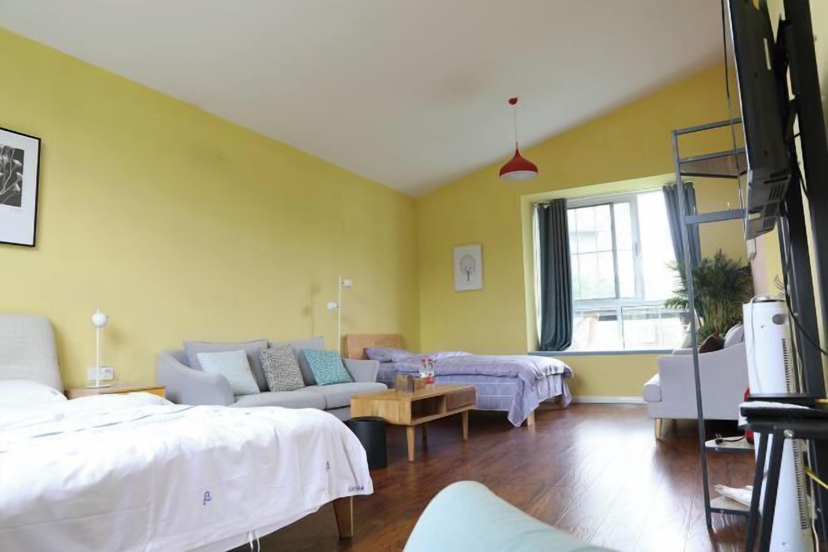 A room with two beds, a sofa, a small table, a TV, and a window.